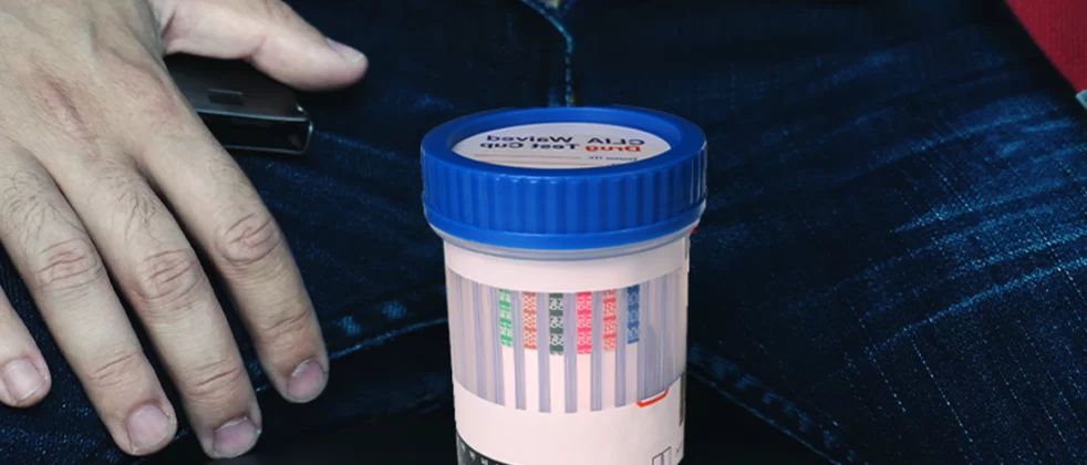 Drug test cup in between guy's pants