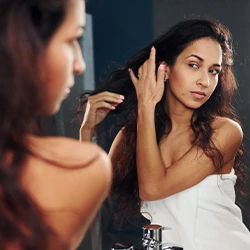 Woman in towel looking at the mirror checking her hair 