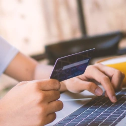 A person holding a credit card in front of a laptop